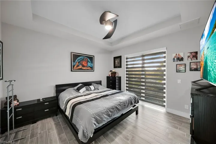 Bedroom featuring ceiling fan, light hardwood / wood-style floors, and a tray ceiling