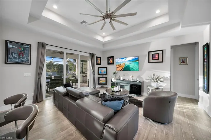 Living room featuring ceiling fan, light wood-type flooring, indoor bar, and a tray ceiling