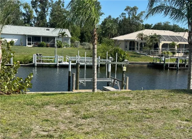 Dock area with boat lift, a water view, and a yard