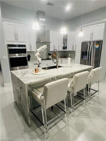 Kitchen with light stone countertops, stainless steel appliances, a kitchen bar, and wall chimney range hood