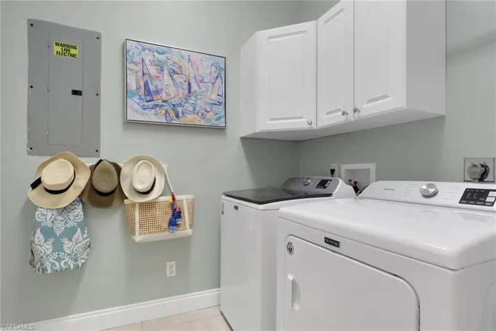 Laundry room with electric panel, cabinet space, separate washer and dryer, and light tile patterned floors
