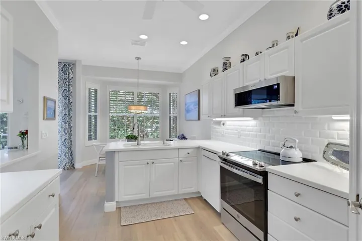 Kitchen with stainless steel appliances, a peninsula, crown molding, white cabinets, and light wood-type flooring