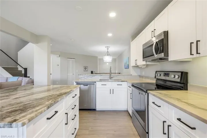 Kitchen with appliances with stainless steel finishes, open floor plan, white cabinets, light stone counters, and light wood finished floors