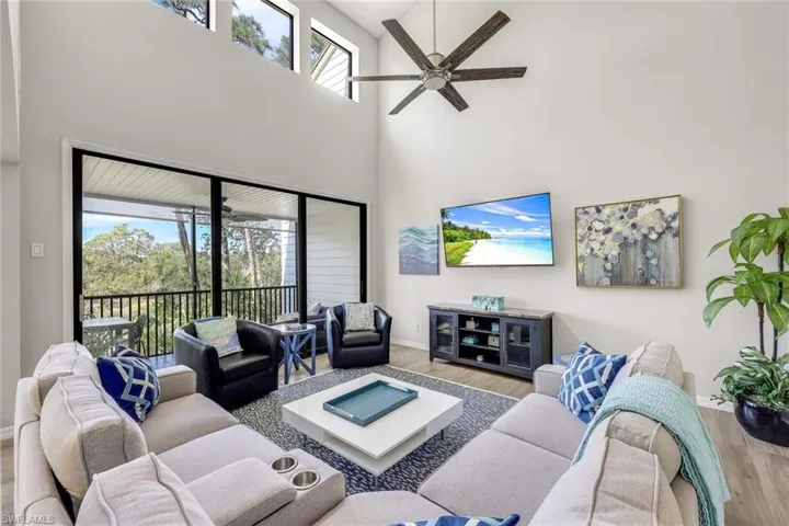 Living area with wood finished floors, plenty of natural light, a ceiling fan, and a towering ceiling