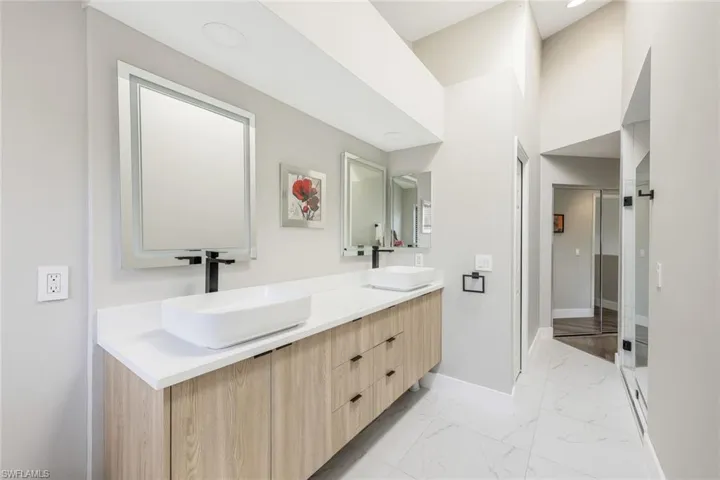 Bathroom featuring double vanity, light marble finish floors, a high ceiling, and a stall shower