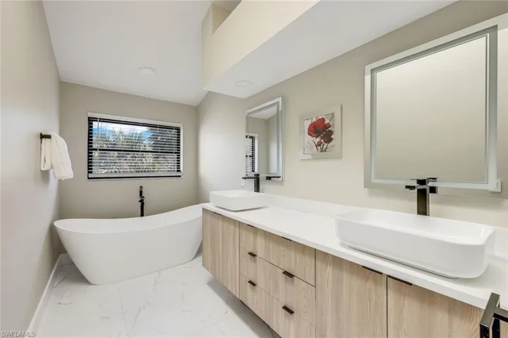 Primary bathroom updated with soaking tub, light marble finish flooring, a soaking tub, and double vanity.