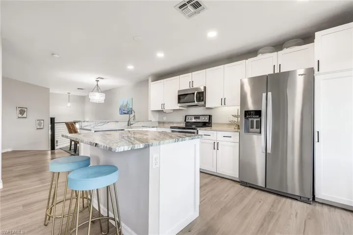 Gorgeous kitchen with stainless steel finishes, a breakfast bar, white cabinets, light wood-style flooring, and recessed lighting