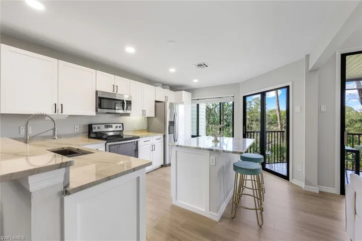 What a gorgeous kitchen!!! Features a breakfast bar, appliances with stainless steel finishes, light stone countertops, white cabinets, and recessed lighting.