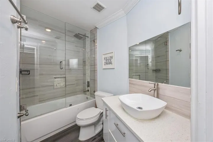 Bathroom featuring vanity, combined bath / shower with glass door, ornamental molding, and dark wood-style floors