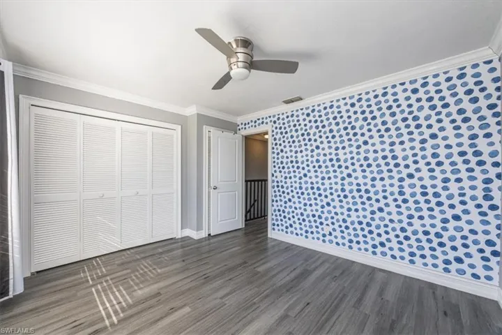 Unfurnished bedroom featuring crown molding, wood finished floors, a closet, ceiling fan, and wallpapered walls