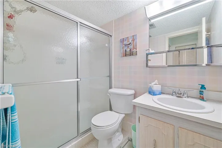 Bathroom featuring a shower with shower door, a textured ceiling, tile patterned floors, toilet, and vanity