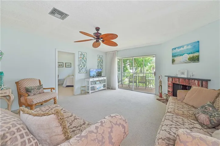 Living room featuring a textured ceiling, carpet flooring, a brick fireplace, and ceiling fan