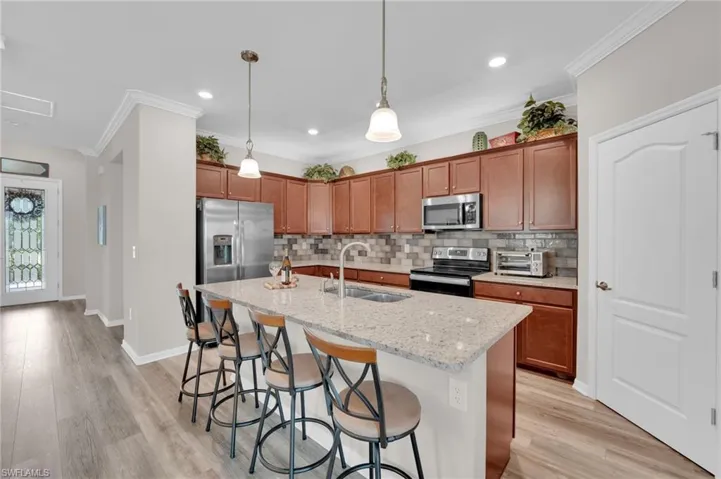 Kitchen featuring crown molding, decorative backsplash, a breakfast bar area, brown cabinets, and appliances with stainless steel finishes