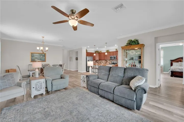 Living area with ceiling fan, ornamental molding, light wood-type flooring, and a chandelier