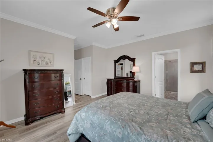 Bedroom with ornamental molding, light wood-type flooring, a ceiling fan, and connected bathroom