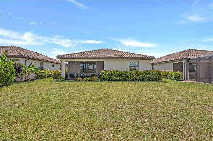 Rear view of property with a sunroom, stucco siding, a lawn, and a tiled roof