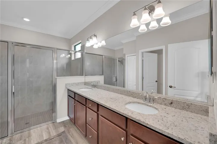 Bathroom with a stall shower, double vanity, ornamental molding, and light wood-style flooring