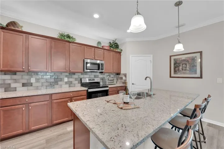 Kitchen featuring backsplash, brown cabinets, appliances with stainless steel finishes, light stone countertops, and crown molding