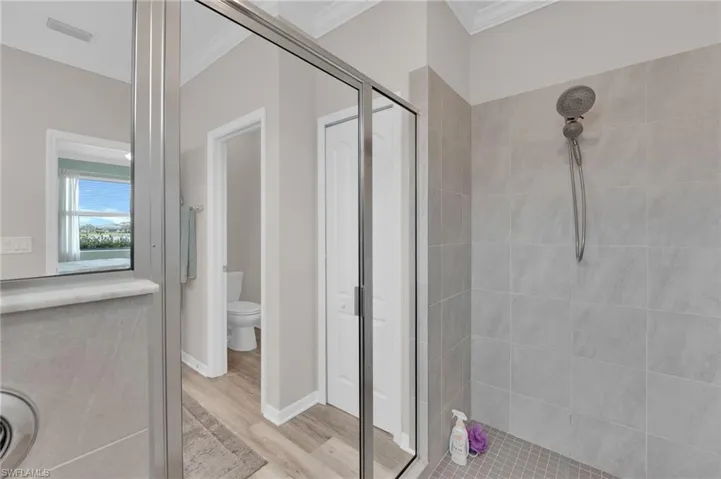 Bathroom featuring a shower stall, ornamental molding, light wood-style floors, and a closet