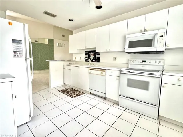 Kitchen with sink, white appliances, light tile patterned floors, and white cabinets