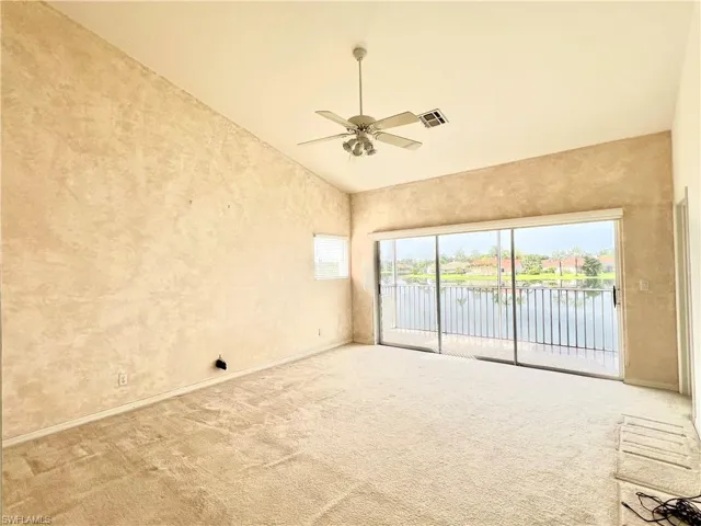 Carpeted empty room with ceiling fan and high vaulted ceiling