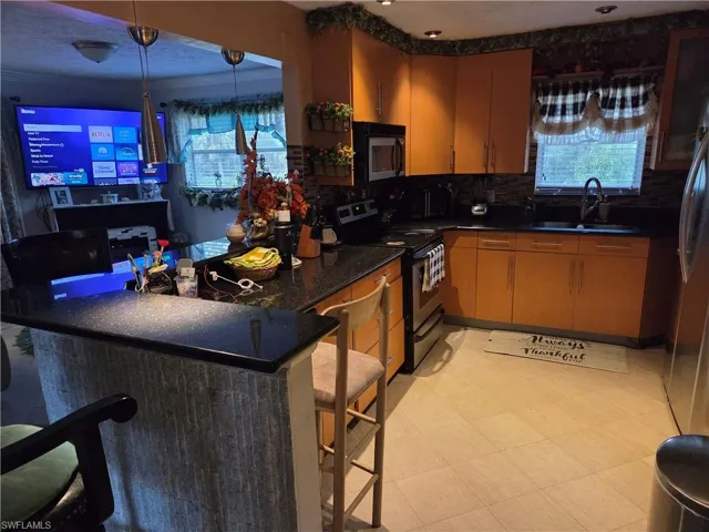 Kitchen upstairs with appliances with stainless steel finishes, a peninsula, a kitchen breakfast bar, brown cabinets, and backsplash