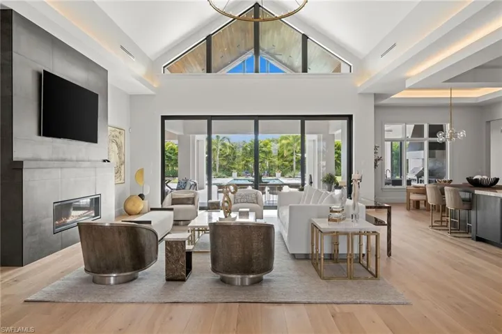 Living room featuring a chandelier, a tiled fireplace, wood finished floors, high vaulted ceiling, and healthy amount of natural light