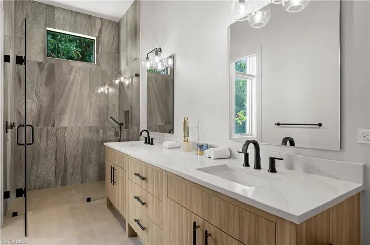 Full bath featuring a marble finish shower and double vanity