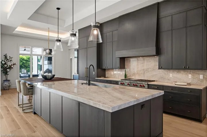 Kitchen with a raised ceiling, wall chimney exhaust hood, a sink, stainless steel gas stovetop, and light wood-type flooring