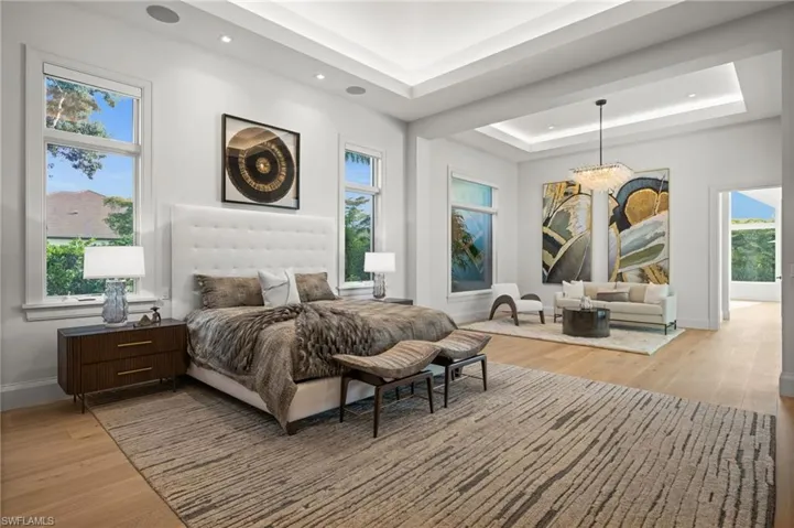 Bedroom with a tray ceiling, light wood finished floors, multiple windows, and recessed lighting