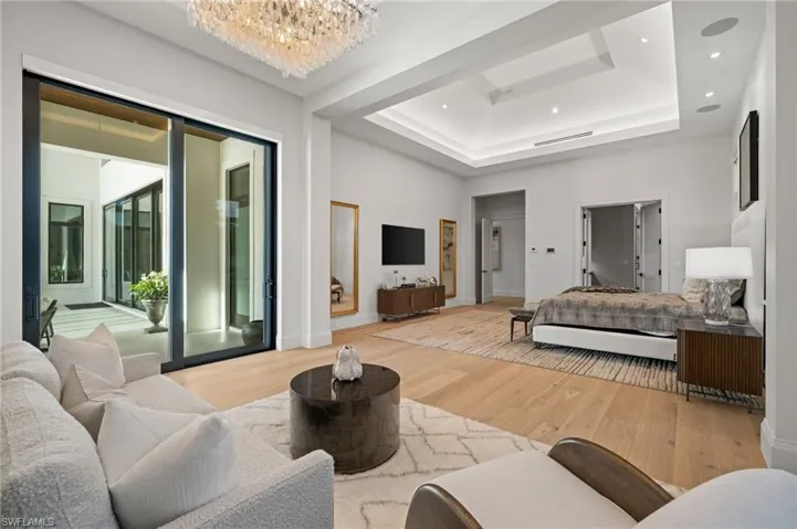 Bedroom with light wood finished floors, access to outside, a chandelier, a tray ceiling, and baseboards