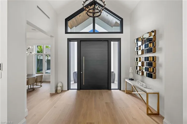 Entrance foyer with wood finished floors, a chandelier, baseboards, and high vaulted ceiling