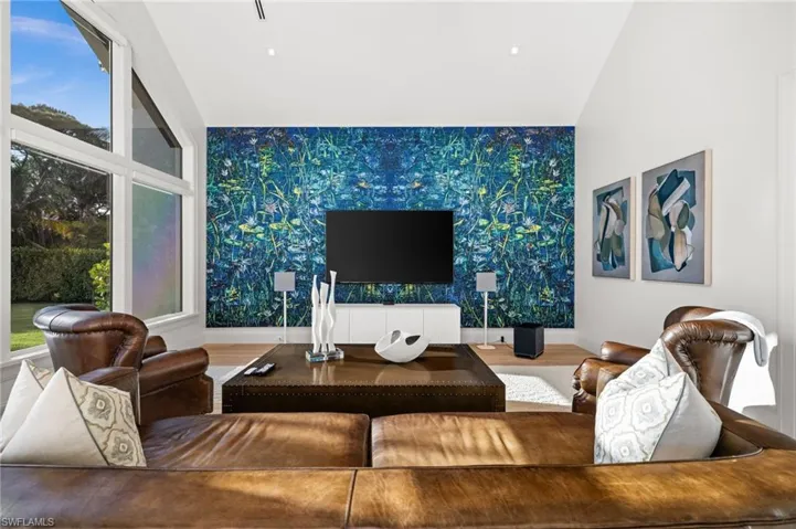 Media area featuring an accent wall, wallpapered walls, baseboards, and wood finished floors