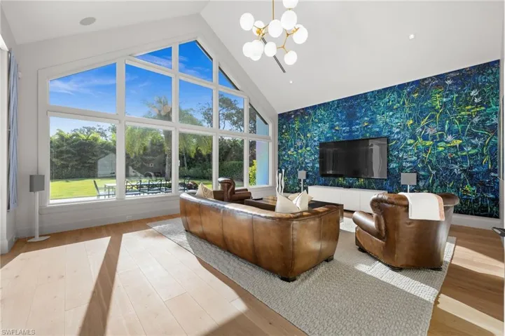 Media area featuring wallpapered walls, an accent wall, a chandelier, baseboards, and wood finished floors