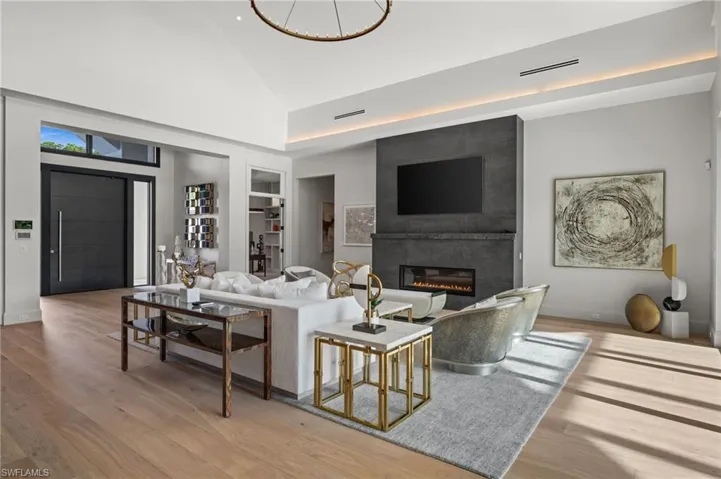 Living room with built in features, wood finished floors, a large fireplace, high vaulted ceiling, and baseboards