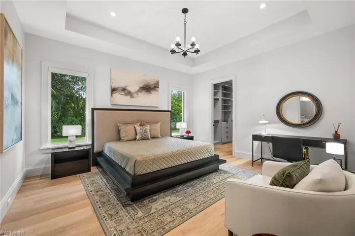 Bedroom with a raised ceiling, a chandelier, light wood finished floors, a walk in closet, and recessed lighting