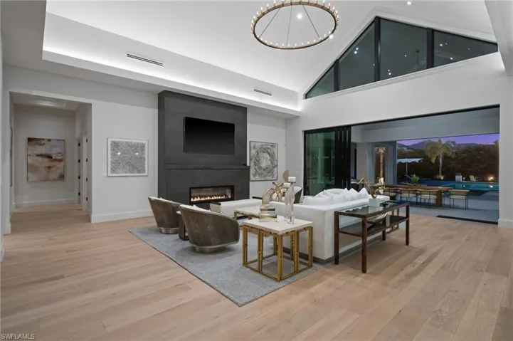 Living area with wood finished floors, a fireplace, high vaulted ceiling, baseboards, and a chandelier
