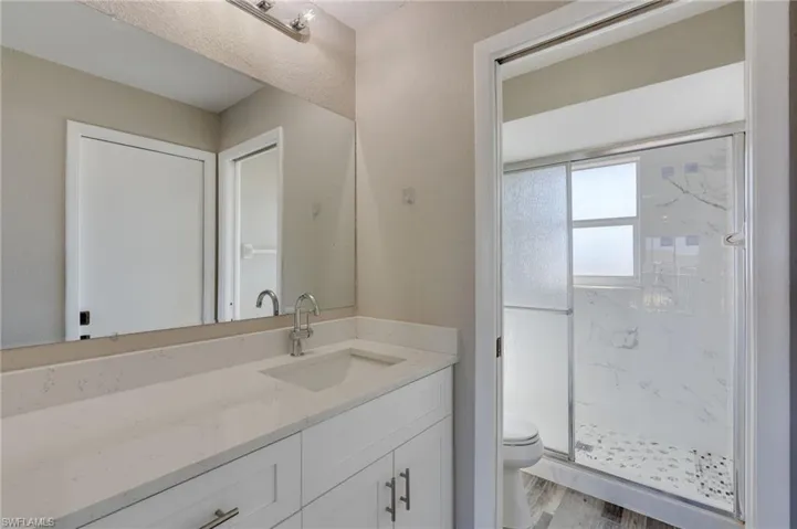 Full bath with vanity, a marble finish shower, and light wood-style flooring