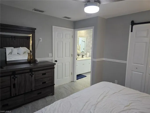 Bedroom with a barn door, ensuite bath, and a ceiling fan