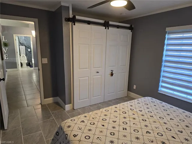 Bedroom with ornamental molding, a barn door, a ceiling fan, and a closet