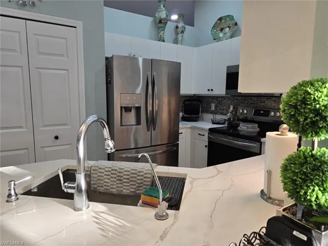 Kitchen featuring stainless steel appliances, white cabinets, decorative backsplash, and light stone counters