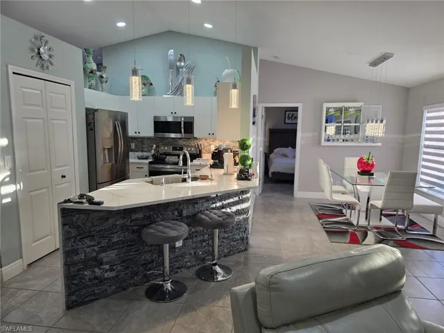 Kitchen featuring stainless steel appliances, hanging light fixtures, a kitchen bar, a peninsula, and light stone countertops