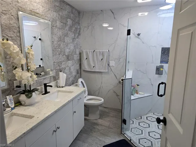 Bathroom featuring double vanity, tile walls, a marble finish shower, and stone wall