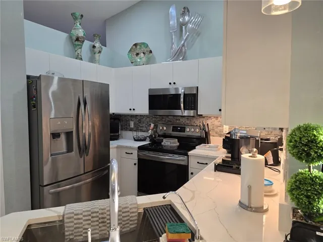 Kitchen with stainless steel appliances, white cabinetry, decorative backsplash, a high ceiling, and light stone countertops
