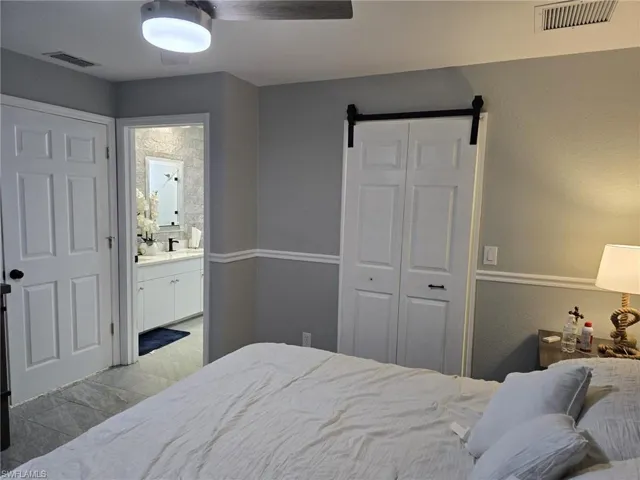 Bedroom with a barn door, ensuite bathroom, a ceiling fan, a closet, and a textured wall