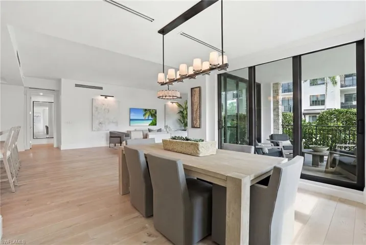 Wood-finish flooring throughout, a modern linear chandelier, and expansive sliding glass doors leading to a private outdoor balcony