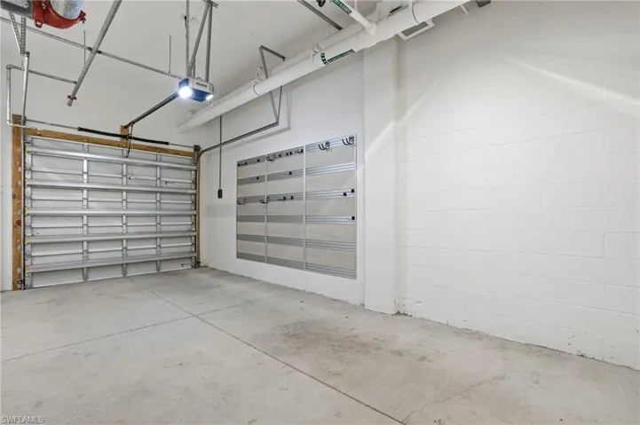 Concrete flooring, overhead garage door, automatic garage door opener, exposed ceiling pipes, white painted block walls