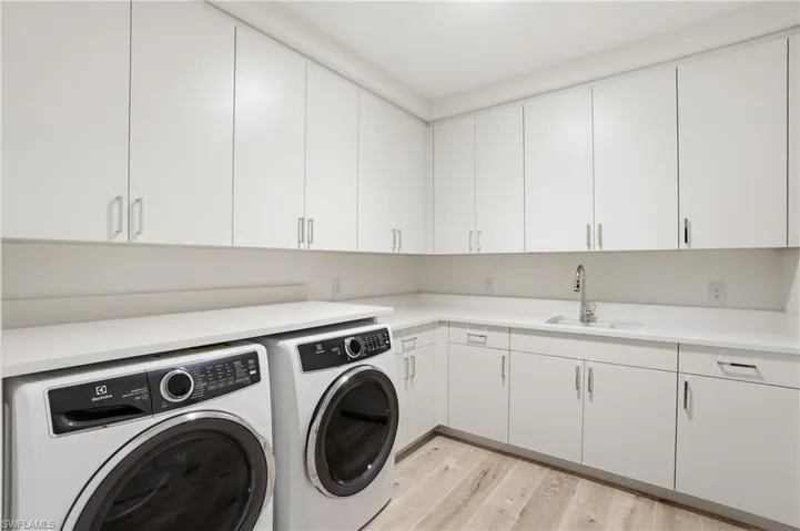 Expansive laundry space featuring extensive white cabinetry, light-toned countertops, an undermount sink with a gooseneck faucet, and wood-finish flooring