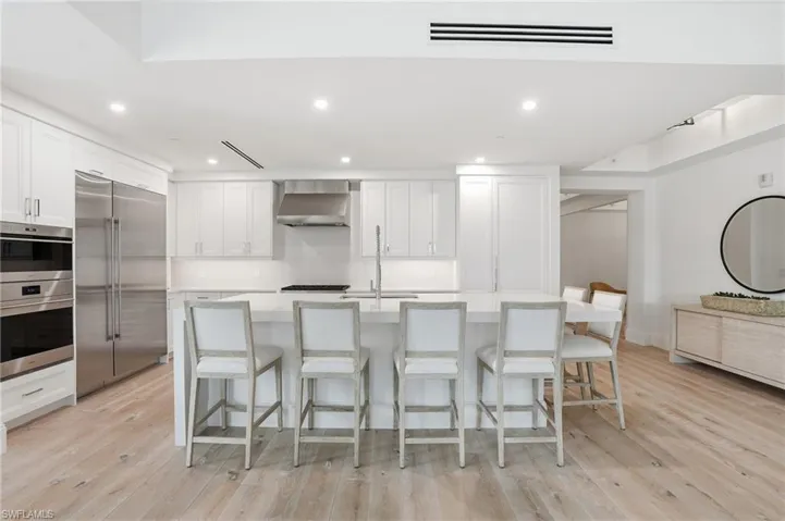 Contemporary kitchen featuring white cabinetry, integrated stainless steel appliances, a center island with counter seating, light wood-finish flooring, and recessed lighting