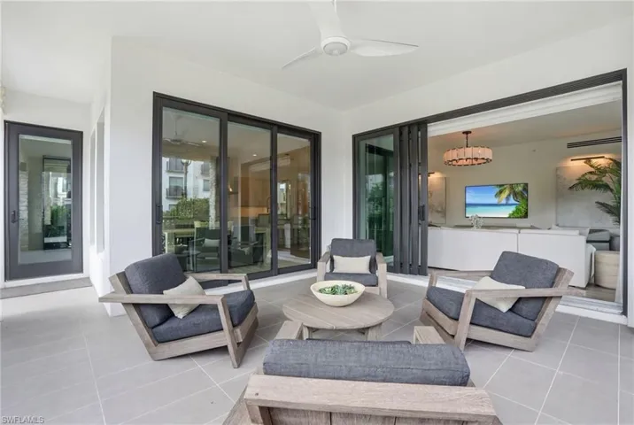 Covered patio with large format tile flooring, black-framed sliding glass doors, a ceiling fan, and a separate glass-paneled door